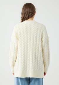 Maglione oversize color crema con motivo a trecce, caratterizzato da un orlo a coste e morbido filato spesso; vista posteriore mostrata.