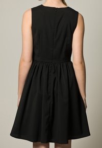 Robe noire sans manches avec un corsage ajusté, une taille froncée et une jupe évasée. Elle possède une fermeture éclair au dos et une texture lisse.