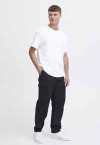 Hvid bomulds T-shirt i afslappet pasform. Sorte cargo bukser med sidelommer. Hvide sneakers. Enkelt design, glat tekstur. Neutral baggrund.