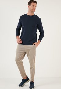 Kék hosszú ujjú póló, texturált anyagból, világos bézs slim-fit nadrággal párosítva, és kék sportcipő fehér talppal.