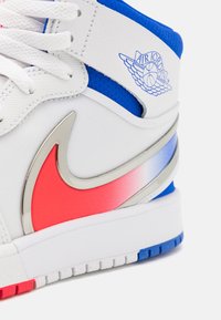 Valge Air Jordani jooksukäpik punase ja hõbedase Nike swooshiga, siniste aktsentide ja sinise "Air Jordan" logoga pahkluuringil.