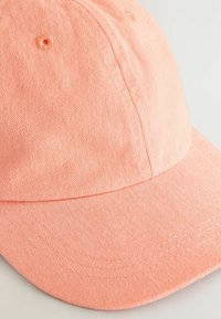 Justerbar cap i solid lyserød stof. Har en buet skygge, tonale syninger og ventilationshuller på toppen.