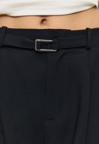Czarne spodnie z szerokim paskiem i srebrną sprzączką. Gładka faktura i dopasowany krój z bocznymi kieszeniami.