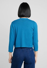 Blue cropped sweater with long sleeves, lightweight texture, round neckline, and ribbed cuffs. Paired with high-waisted dark denim jeans.