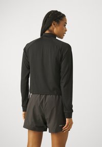 Maglietta atletica nera a maniche lunghe con un design cropped, caratterizzata da maniche raglan. Abbinata a pantaloni corti scuri, mostrando un look minimalista.