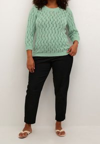 Pull vert menthe clair en tricot avec un motif texturé en losanges, manches 3/4, et col rond, associé à un pantalon noir fuselé et des sandales.