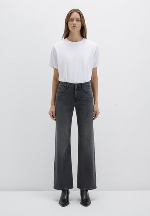 White short-sleeve t-shirt paired with high-waisted, wide-leg dark grey jeans. Model wear black ankle boots. Simple, modern fit.