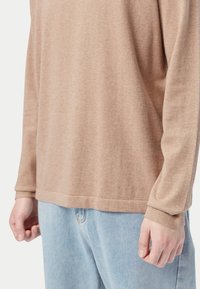 Hellbraunes Langarmhemd aus weichem Stoff, mit lockerer Passform und gerippten Bündchen, kombiniert mit hellblauen Jeans.