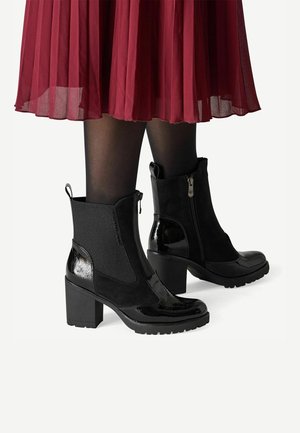 Zwarte enkellaarsjes met blokhak, zijrits en aantreklus, gedragen met zwarte panty's en een rode geplooide rok.
