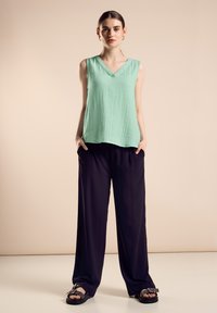 Top sin mangas de color verde menta con escote en v y tela texturizada, combinado con pantalones negros holgados y sandalias planas negras. Diseño simple y moderno.