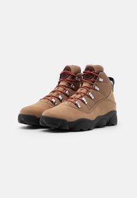 Braune Wanderschuhe mit einem Obermaterial aus Wildleder und Mesh, roten Schnürsenkeln, silbernen Ösen und schwarzen Gummisohlen. Mittelhohe Ausführung für Unterstützung des Knöchels.