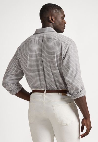 Siva karo s karirasto vzorcem, z zavihanimi rokavi, kombinirana z belimi hlačami in rjavim pasom. Srajca ima klasičen ovratnik.