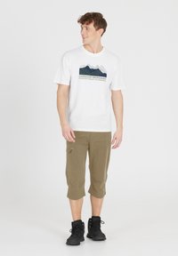 Vit bomullströja med en bergsgrafik och text, tillsammans med olivgröna capribyxor med en ficka med dragkedja och en avslappnad passform. Svarta kängor.