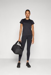 Camiseta atlética negra y leggings, combinados con zapatillas deportivas negras, sosteniendo una bolsa de deporte negra. Diseño simple y ajustado, textura suave.