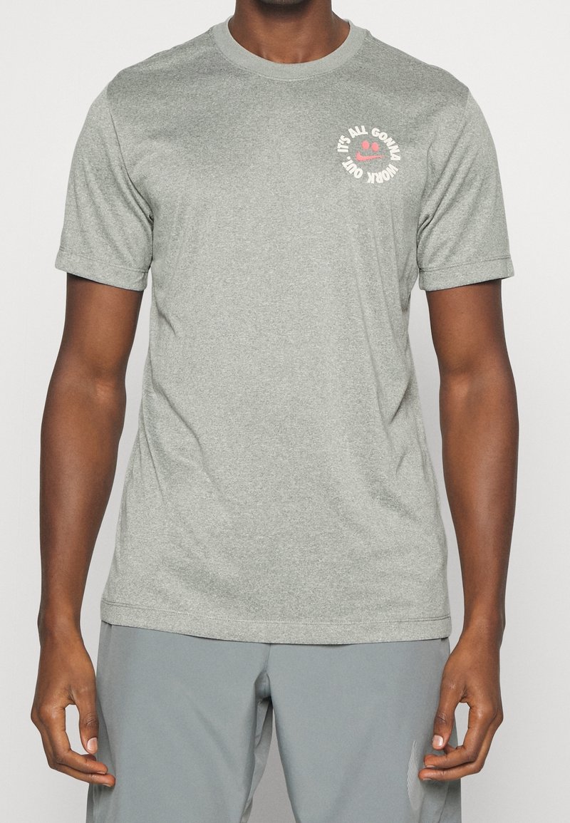 T-shirt gris à manches courtes en tissu doux, avec un col rond et un texte graphique rose accompagné d'un visage souriant sur le côté gauche de la poitrine.