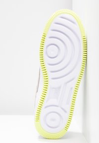 Semelle extérieure de chaussure blanche avec une bordure en caoutchouc épaisse, texturée, de couleur verte et jaune. Présente des motifs circulaires et un logo Nike bien visible.