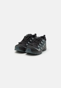 Zapatillas deportivas negras con una parte superior texturizada, que presentan rayas reflectantes, un collar acolchado y una suela resistente para mayor tracción.