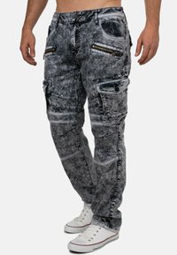 Jeans cargo grigi con finitura sbiadita, dotati di molteplici tasche con zip, cuciture a contrasto e design a gamba dritta. Indossati con sneakers bianche.