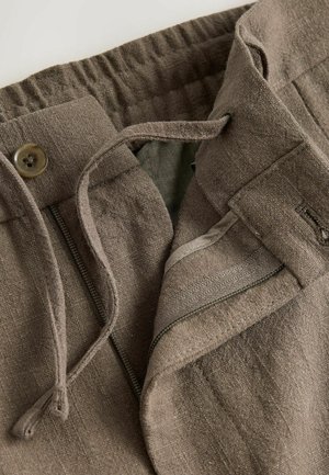 Brune linned bukser med en lynlåslomme, elastisk talje, snøre og knaplukning med en tekstureret overflade.