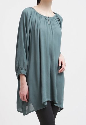 Blusa a maniche lunghe color turchese con scollo rotondo, dettagli arricciati e vestibilità ampia, realizzata in tessuto leggero e fluente.