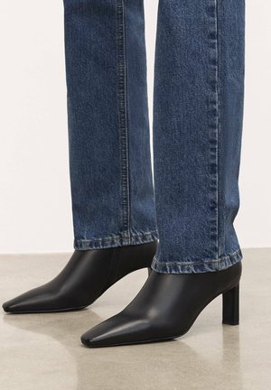 Stivali alla caviglia in pelle nera con punta a punta e tacco spesso, abbinati a jeans in denim scuri a gamba dritta con cuciture a contrasto.