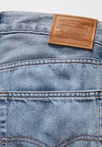 Gros plan de la poche arrière d’un jean en denim bleu clair avec un patch en cuir marron Levi Strauss & Co. cousu au-dessus de la poche.