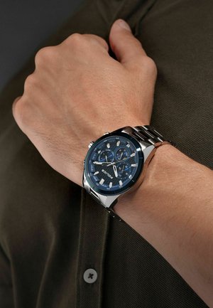 Montre-bracelet en acier inoxydable avec un large cadran bleu, des accents blancs, des fonctionnalités de chronographe et un bracelet en maillons métalliques argentés.