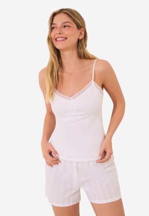 Witte camisole met kant afwerking en knoopdetails, gecombineerd met witte shorts met een subtiel textuurpatroon, beide gemaakt van zachte stof.