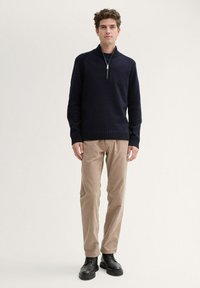 Marineblauer Zip-Hoodie mit geripptem Saum, kombiniert mit braunen Cordhosen und schwarzen Schnürstiefeln. Das Outfit besticht durch ein einfaches, lässiges Design.