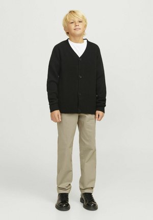 Czarny kardigan z dekoltem w serek, pięcioma guzikami, prążkowanymi mankietami i dołem, w połączeniu z beżowymi spodniami i czarnymi butami. Pod spodem gładka biała koszulka.