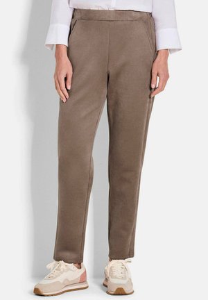 Braune, taillierte Hose aus weichem Stoff mit glatter Textur, ausgestattet mit seitlichen Taschen und hohem Bund, kombiniert mit hellen Sneakers.