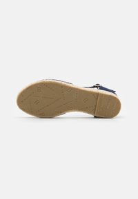 Buty w stylu espadryli z solidną, owiniętą jute'ą podeszwą, górą z granatowego płócienia i tłoczonym logo. Posiadają klamrę do bezpiecznego dopasowania.