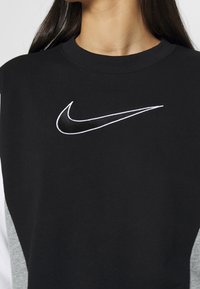 Black sweatshirt with white Nike swoosh logo on the chest worn by a person with long dark hair and light skin.