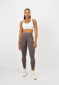 Sostén deportivo azul claro con cremallera frontal y leggings grises de cintura alta, combinados con zapatillas ligeras, sobre un fondo neutro.