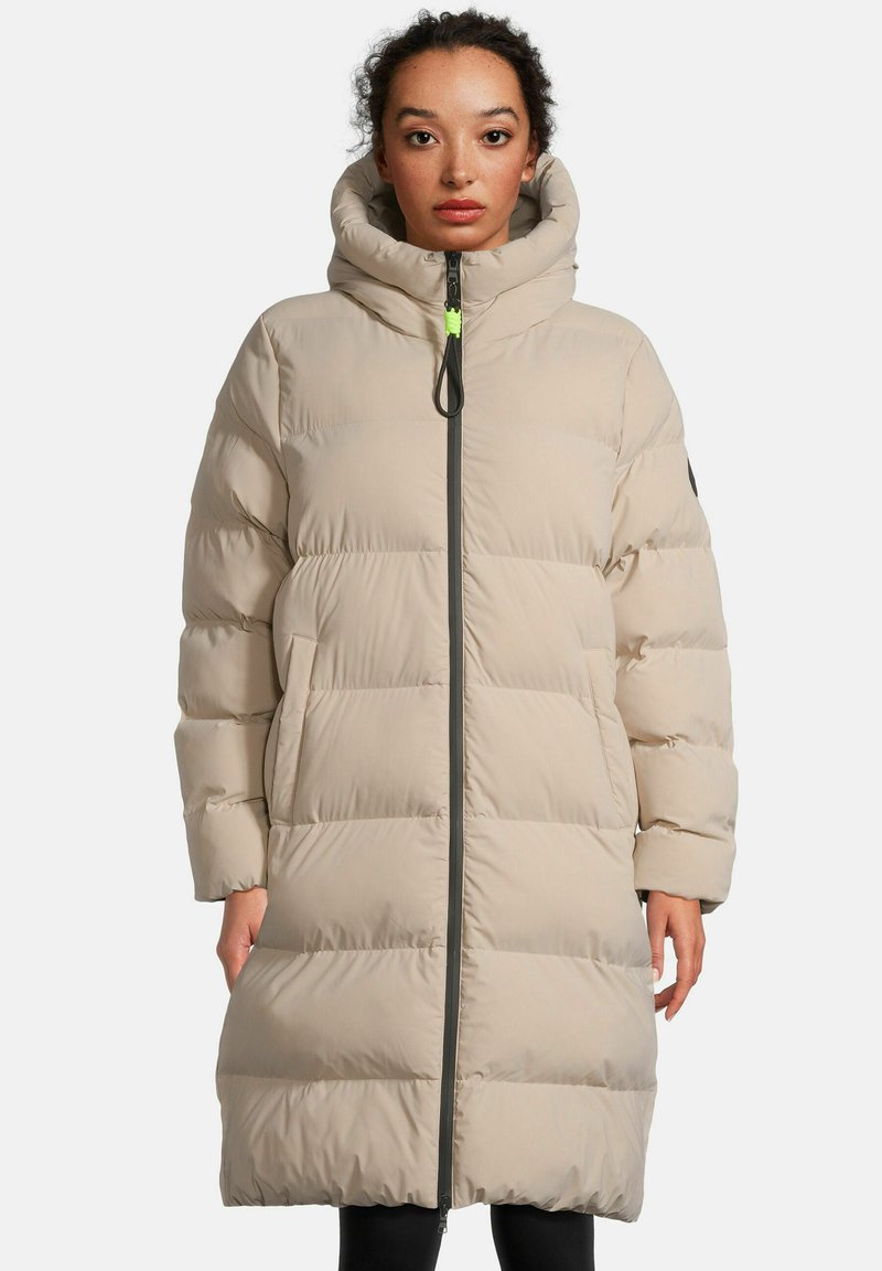 Beige gepolsterter langer Mantel mit hohem Kragen, Frontreißverschluss und Taschen; verfügt über eine strukturierte Oberfläche und einen schwarzen Akzent an einem Ärmel.