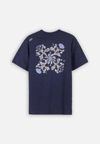 T-shirt bleu marine avec un motif floral symétrique dans des nuances de beige et de bleu clair au dos, comportant une étiquette Oxbow près de l'épaule.