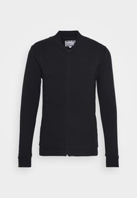 Giacca nera con zipper, colletto alto, polsini a coste, due tasche anteriori e dettaglio del logo impresso sul petto. Tessuto con texture liscia.