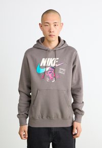 Grå hættebluse med lomme foran, der har et farverigt Nike-logo og en tegneserie-grafik. Blødt fleece-materiale med ribbede manchetter.