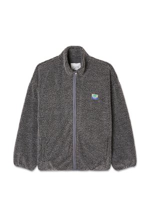 Tumši pelēka pilna rāvējslēdzēja flīsa jaka ar teksturētu audumu, stāvošu apkakli, elastīgiem aprocēm un nelielu zili zaļu uzlīmi uz kreisā krūšu daļas.