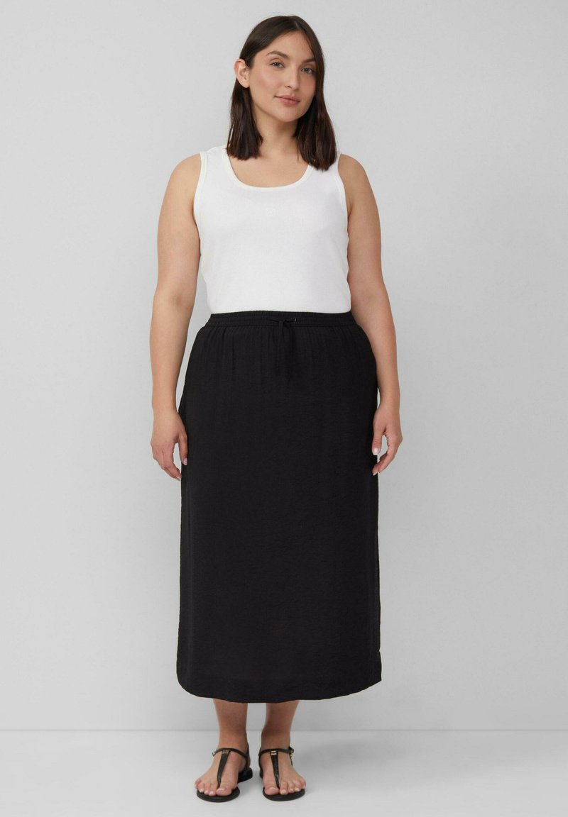 Zwarte maxi-rok met een trekkoord in de taille, gecombineerd met een witte tanktop. De stof lijkt lichtgewicht en gestructureerd. Platte sandalen maken de look compleet.