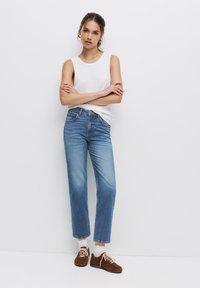 Ljusblå, raka jeans med en blekt tvätt, kombinerat med en vit linne och bruna sneakers. Minimalistisk design, inga synliga mönster.