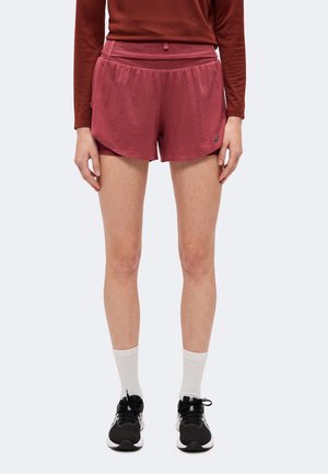 Personne portant un short de sport bordeaux avec un haut assorti, des chaussettes blanches et des chaussures de course noires, debout devant un fond uni.