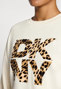 Krém színű pulcsi nagy "DKNY" logóval, mely leopárdmintás. Kerek nyakkivágás ribbelt gallérral és puha anyagtextúrával.