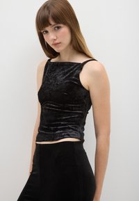 Top corto in velluto nero con scollo quadrato, spalline sottili e design aderente che mette in risalto una trama liscia.