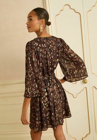 Rochie maro transparentă, cu croială lejeră, imprimeu leopard metalic dispersat și mâneci bufante. Se încheie cu talie strânsă și tiv evazat.