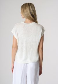 Camicia leggera e a maniche corte in bianco sporco, con una vestibilità rilassata e un tessuto morbido e testurizzato. Collo rotondo con bordi arrotolati.