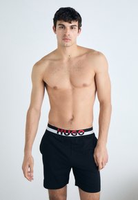 Čierne boxerky s červeným a bielym pásom s logom "HUGO", s jednoduchým dizajnom a jemnou, hladkou textúrou.
