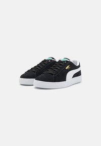 Black suede sneakers with white rubber soles, featuring black laces and a white side stripe. Notable details include a small gold logo.