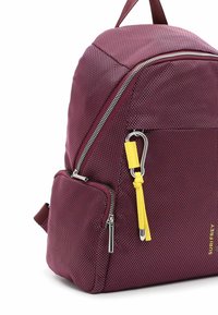 Sac à dos en textile bordeaux avec une forme structurée, doté d'une fermeture éclair argentée, d'une étiquette d'accent jaune et d'une poche avant avec une petite fermeture éclair.