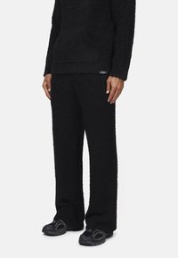 Set di lounge in pile nero caratterizzato da un hoodie texture, dal fit morbido, con tasca frontale e pantaloni a gamba larga coordinati. Entrambi hanno una finitura soffice.